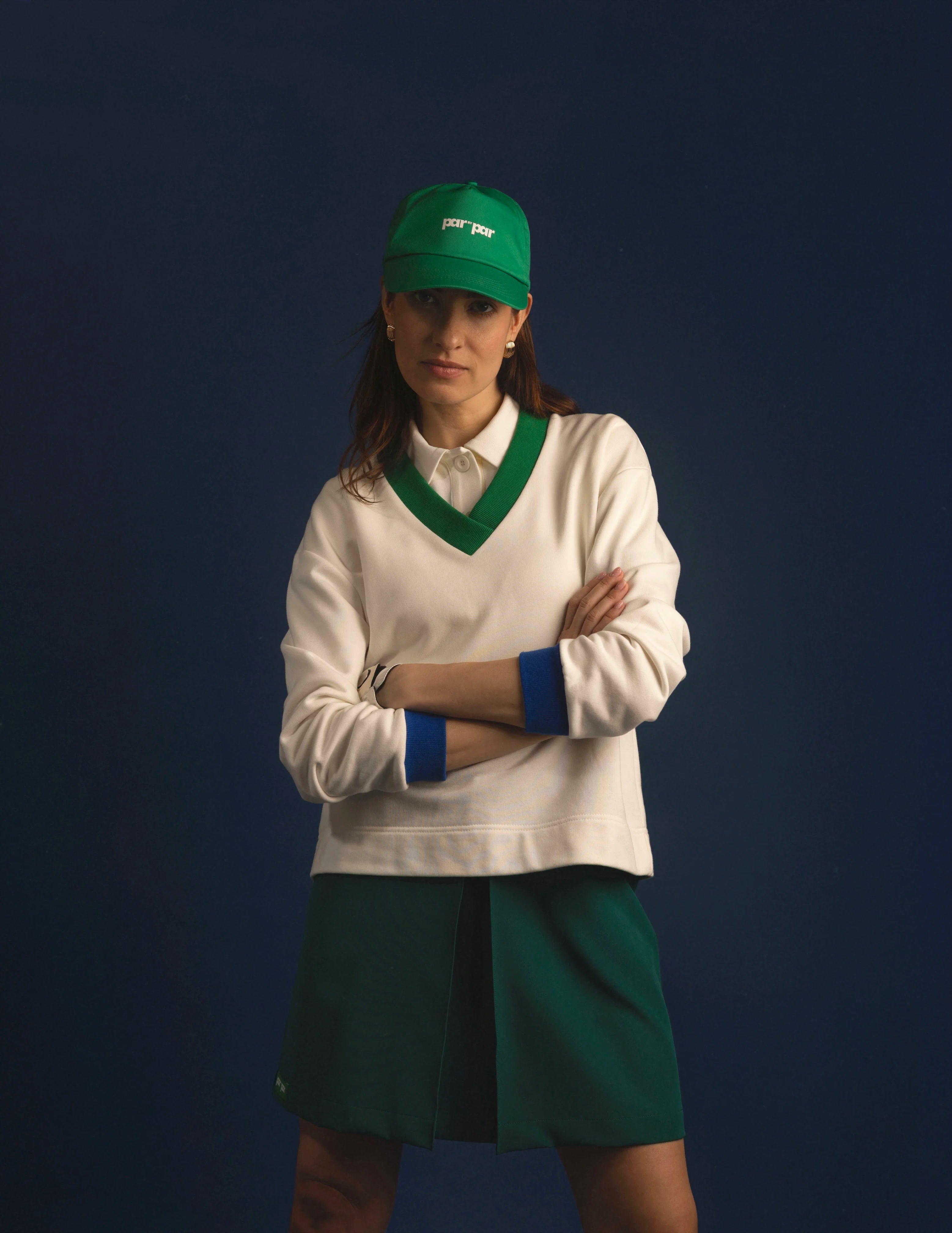 Person wearing a white sweater with green accents and a green cap against a dark background